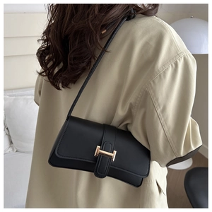 Detail of a chic black underarm bag with a golden H buckle worn on the shoulder