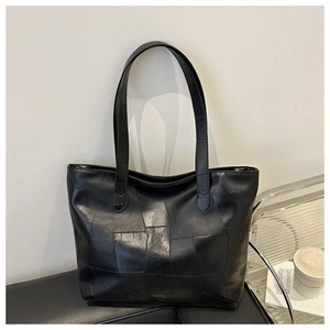 Detail of a black leather tote bag featuring a geometric patchwork design and dual straps