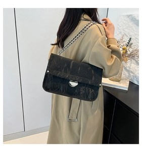 Detail of black wrinkled texture shoulder bag with silver chain strap on khaki coat