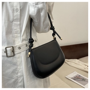 Detail of black leather shoulder bag featuring unique knotted strap and golden accents