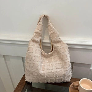 Minimalist beige shoulder tote bag with 3D frayed square texture on a wooden table