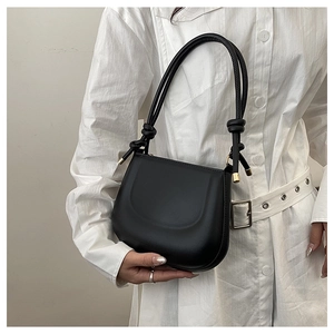 Detail of minimalist black matte leather saddle bag with long knotted handle and gold accents