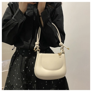 Detail of light beige PU shoulder bag featuring a knotted strap and gold metal hardware