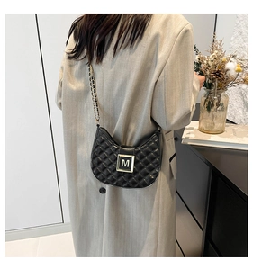 Close-up of black quilted half-moon bag with metallic M-buckle and chain strap
