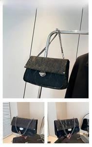 Detail view of black pleated underarm bag featuring silver chain and metal buckle