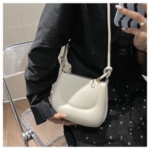 Close-up of white leather shoulder bag featuring knotted strap and sleek zipper detail
