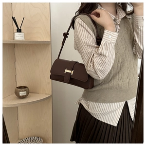 Detail of a deep brown leather baguette bag featuring a gold H-shaped metallic buckle