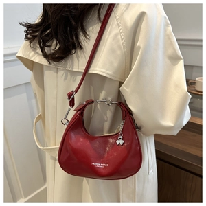 Red glossy crescent shoulder bag with metallic charms shown on a trench coat model