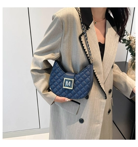 Detail of navy quilted leather crossbody bag with gold M buckle worn on a beige blazer