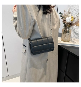 Detail of a black quilted leather crossbody bag with silver chain strap worn by a model