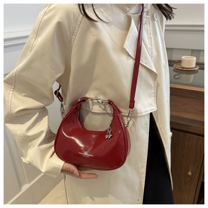 Detail of red crescent shoulder bag in glossy leather worn with a beige coat