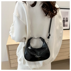 Close-up of black patent leather crescent bag with white bow charm and metal strap