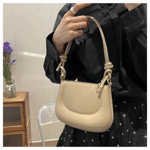 Macro detail of creamy beige moon bag with decorative knotted shoulder strap and gold hardware