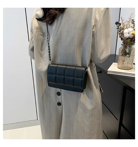 Close-up of a black quilted leather crossbody bag with chain strap on a grey coat