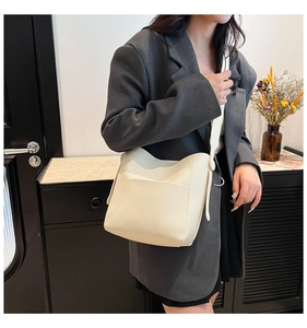 Close-up of ivory pebble-textured bucket bag showing front pocket and wide shoulder strap
