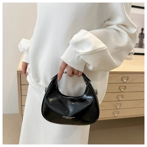 Detail of a black glossy leather crescent bag featuring a stylish metal chain and logo text