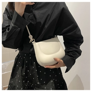 Close-up of cream shoulder bag with knot detail and textured finish on a black dress