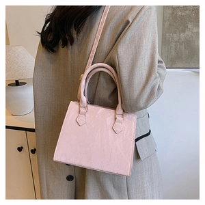 Close-up of a pink patent leather crossbody bag showing glossy texture and gold hardware
