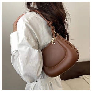 Detail of a brown leather crescent shoulder bag featuring a unique leather knot on the strap