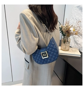 Detail of navy crescent bag showing quilted pattern and gold M-buckle on a shoulder strap
