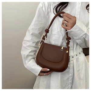 Close-up of brown faux leather saddle bag with decorative knotted strap and gold hardware