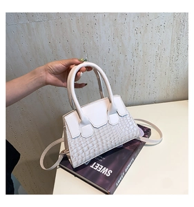 Dettaglio di una mini borsa bianca a rilievo coccodrillo su un libro viola
