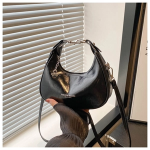 Detail of glossy black crescent bag with silver clover charm and adjustable strap