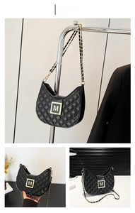 Detail of black quilted leather shoulder bag with gold M-buckle and chain strap