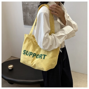 Detail of yellow tote bag featuring green Support lettering and adjustable side drawstring