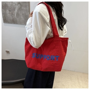 Detail of red drawstring canvas tote bag with blue support letter print on shoulder strap