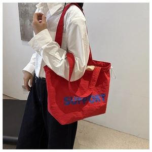 Detail of red canvas tote bag with SUPPORT blue lettering and drawstring closure detail