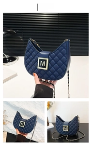 Close-up of blue quilted hobo bag with gold M-buckle and woven chain shoulder strap