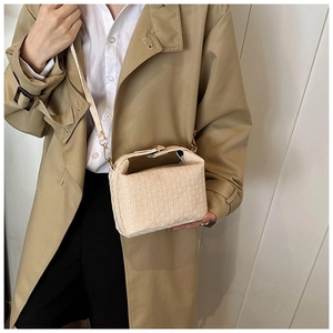 Detail of beige structured handbag with geometric textured finish and metal strap clip