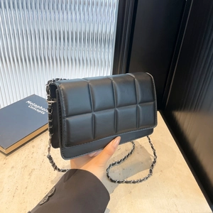 Minimalist black quilted crossbody bag with metal chain strap held by a person