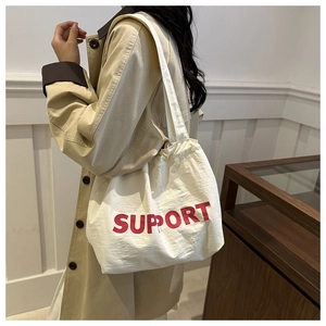 Close-up of a white canvas tote bag with bold red SUPPORT print on beige trench coat