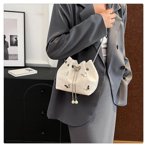 White drawstring bucket bag with silver butterfly charm and pearl tassels on a chain strap