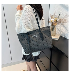 Close-up of dark grey tote bag with bow prints worn by a model in a casual setting