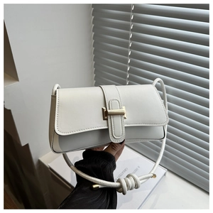 Detail of white baguette bag with gold metal buckle and decorative knotted shoulder strap