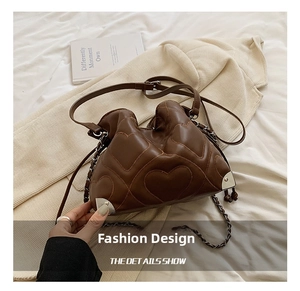 Close-up of brown leather bucket bag with heart stitching and metal chain detail