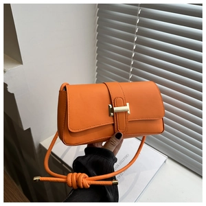 Detail of a bright orange baguette bag featuring a gold buckle and knotted cord strap