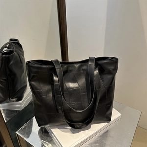 Large black leather tote bag with patchwork texture shown on a reflective mirror surface