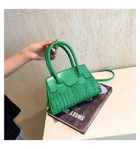 Dettaglio di una mini borsa verde acceso con trama a coccodrillo e manici tondi