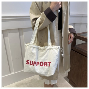 Detail of white canvas tote bag with bold red SUPPORT print and drawstring closure