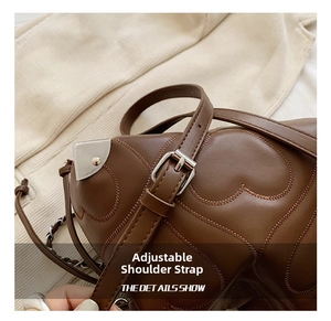 Close-up of heart-stitched brown leather bag with adjustable silver buckle strap