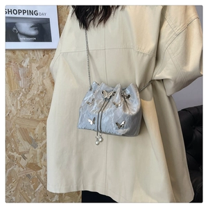 Detail of silver textured bucket bag with metallic butterfly accents and pearl drawstring