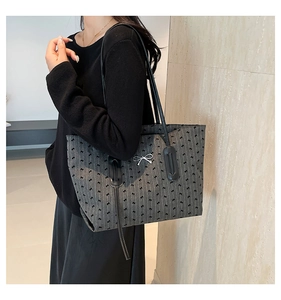 Detail of grey tote bag with black bow print and silver bow charm in a home setting