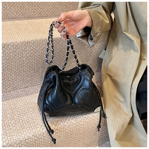 Detail of black heart-quilted tote bag featuring silver chain strap and drawstring closure