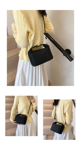 Detailed close-up of a black woven textured crossbody bag with gold metallic lock and handle