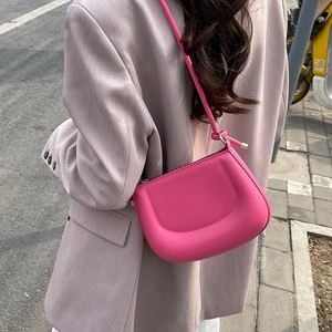 Rose pink saddle shoulder bag with matte finish and minimalist arc design on urban street
