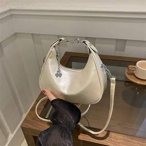 Chic beige crescent shoulder bag with glossy finish and silver clover charm detail